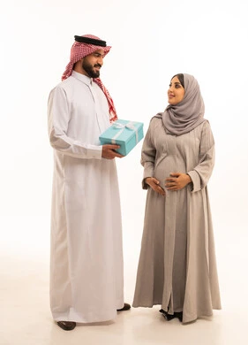 الألفة والمحبة بين الزوجين، مشاركة وتقديم الهدايا في الأعياد والمناسبات العائلية, بورترية لرجل عربي خليجي سعودي يرتدي الثوب الابيض و الشماغ يقدم لزوجته صندوق الهديه، مفهوم الحمل و الانجاب, الجسم بالطول الكامل، خلفية بيضاء