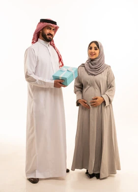Sharing and giving gifts during holidays and family occasions, a portrait of a Saudi Arabian Gulf man wearing a white thobe and a ghutrah presenting a gift box to his wife, the concept of pregnancy and childbirth, intimacy and love between spouses, full-body, white background. Sharing and giving gifts during holidays and family occasions, a portrait of a Saudi Arabian Gulf man wearing a white thobe and a ghutrah presenting a gift box to his wife, the concept of pregnancy and childbirth, intimacy and love between spouses, full-body, white background.