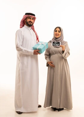 تقديم الهدايا في العيد والمناسبة الخاصة، بورترية لرجل عربي خليجي سعودي يرتدي الثوب الابيض و الشماغ يحمل صندوق الهدية برفقه زوجته ، امراه حامل عربيه خليجيه سعودية تحمل بيديها اشعه السونار ، مفهوم الحمل و الانجاب، الجسم بالطول الكامل، خلفية بيضاء