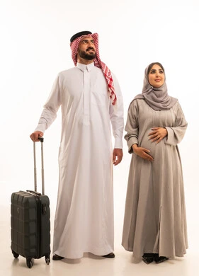 النظر للاعلى الى شيء ما، قضاء أوقات ممتعة في الإجازة, الاستمتاع بالسفر و الرحلات الصيفية,بورترية لرجل عربي خليجي سعودي يرتدي الثوب الابيض و الشماغ يمسك بيده حقيبة السفر برفقة زوجته, مفهوم الحمل و الانجاب, صورة للجسم بالطول الكامل, خلفية بيضاء