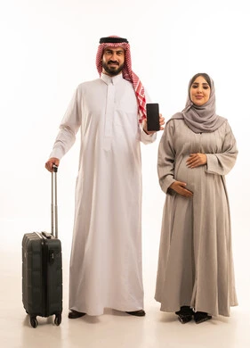 قضاء أوقات ممتعة في الإجازة, الاستمتاع بالسفر و الرحلات الصيفية, بورترية لرجل عربي خليجي سعودي يرتدي الثوب الابيض و الشماغ يمسك بيده حقيبة السفر برفقة زوجته, مفهوم الحمل و الانجاب،عرض شاشة سوداء فارغه عبر الجوال, صورة للجسم بالطول الكامل, خلفية بيضاء