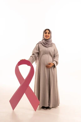 الحملة التوعويه بالامراض الخبيثه، بورتريه لامرأة عربية خليجية سعودية محجبة ترتدي العباءة تمسك شعار التوعيه بالكشف المبكر لسرطان الثدي، النظر للكاميرا بتعابير السرور، مفهوم الحمل و الانجاب، الجسم بالطول الكامل، خلفية بيضاء