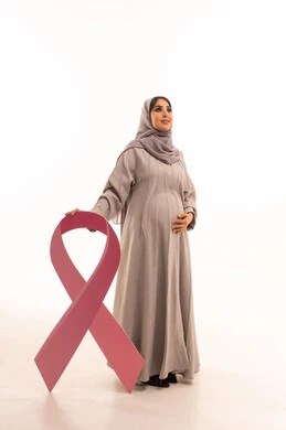 اليوم العالمي للتوعية بالامراض الخبيثة، بورتريه لامرأة عربية خليجية سعودية محجبة ترتدي العباءة تنظر الى للاعلى تمسك شعار التوعيه بالكشف المبكر لسرطان الثدي، مفهوم الحمل و الانجاب، الجسم بالطول الكامل، خلفية بيضاء