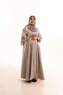 المداومة على شرب المياه، الشعور بالعطش والجفاف، المحافظة على سلامة الجهاز المناعي للجسم، بورتريه لامراة عربيه خليجيه سعودية ترتدي العباءة و الحجابتمسك بيديها زجاجة بلاستيكية صغيرة، مفهوم الحمل و الانجاب، الجسم بالطول الكامل، خلفية بيضاء