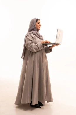 Accomplishing tasks and work, remote work, using a modern and advanced technical device, the concept of pregnancy and childbirth, a side portrait of a Saudi Arabian Gulf woman wearing a hijab and an abaya working on a laptop, full body, white background.