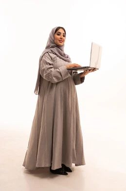 العمل عن بعد, استخدام جهاز تقني حديث ومتطور، مفهوم الحمل و الانجاب، بورتريه من الجانب لامرأة عربية خليجية سعودية محجبة ترتدي العباءة تعمل على جهاز الحاسوب المحمول, انجاز المهام والأعمال, الجسم بالطول الكامل، خلفية بيضاء
