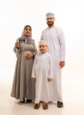 إجراء فحص دوري للجنين باستخدام الأشعة الصوتية، مفهوم الحمل و الانجاب، بورترية لامراة حامل عربيه خليجيه عمانية ترتدي العباءة و الحجاب تحمل بيديها اشعه السونار برفقة ابنها و زوجها، الجسم بالطول الكامل، خلفية بيضاء