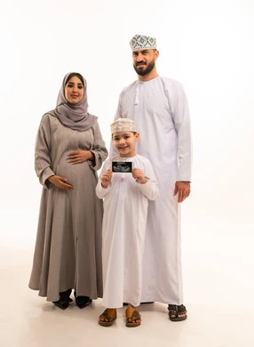 استخدام الأشعة فوق الصوتية لمتابعة الحمل، النظر للكاميرا بتعابير السعادة و السرور، الترابط الأسري والعاطفة بين أفراد العائلة، بورترية لولد عربي خليجي عماني يرتدي الدشداشة و الكمة يمسك بيديه اشعه السونار برفقة والدية ، الجسم بالطول الكامل، خلفية بيضاء
