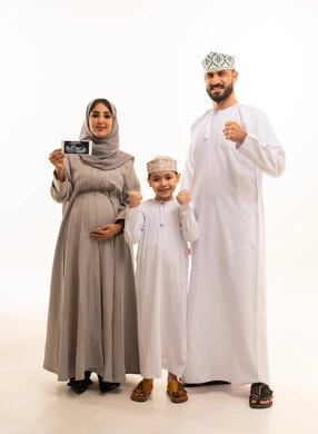 تعابير الفوز و تحقيق النجاح، إجراء فحص دوري للجنين باستخدام الأشعة الصوتية، مفهوم الحمل و الانجاب، بورترية لامراة حامل عربيه خليجيه عمانية ترتدي العباءة و الحجاب تحمل بيديها اشعه السونار برفقة ابنها و زوجها، الجسم بالطول الكامل، خلفية بيضاء