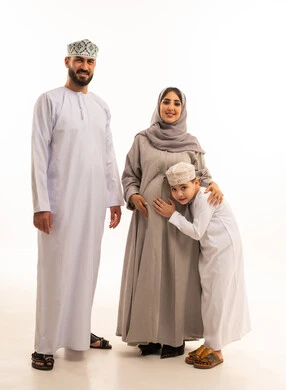 مفهوم الترابط الأسري ، الشوق والارتباط بالجنين القادم، بورترية لولد عربي خليجي عماني يرتدي الدشداشة و الكمه يضع رأسه على بطن والدته برفقة ابيه ، ايماءات السعادة و السرور، الجسم بالطول الكامل، خلفية بيضاء
