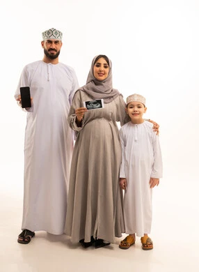 A black screen displayed on a mobile phone, using sonar technology to examine the fetus inside the womb, a portrait of an Arab Gulf Omani pregnant woman wearing an abaya and hijab holding a sonar image in her hands accompanied by her husband and son, the concept of pregnancy and childbirth, gestures of happiness and joy, full-body image, white background.