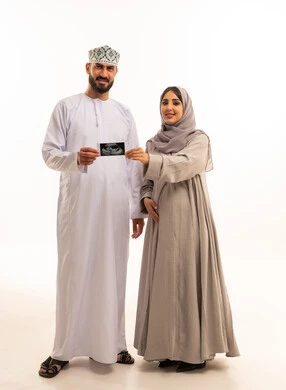 Checking the child's safety using ultrasound, a portrait of an Arab Gulf Omani man wearing a dishdasha and kumma holding a sonar beam with his wife, the concept of pregnancy and childbirth, gestures of happiness and joy, full-body, white background.