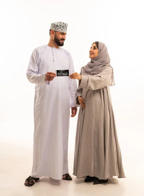 إجراء تصوير طبي لمتابعة نمو الجنين، بورترية لرجل عربي خليجي عماني يرتدي الدشداشة و الكمة يمسك بيديه اشعه السونار ينظر الى زوجته، مفهوم الحمل و الانجاب، ايماءات السعادة و السرور، الجسم بالطول الكامل، خلفية بيضاء