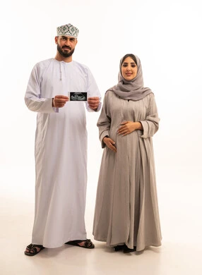 متابعة حالة الجنين عبر فحص الأشعة فوق الصوتية، بورترية لرجل عربي خليجي عماني يرتدي الدشداشة و الكمة يمسك بيديه اشعه السونار برفقه زوجته، مفهوم الحمل و الانجاب، ايماءات السعادة و السرور، الجسم بالطول الكامل، خلفية بيضاء