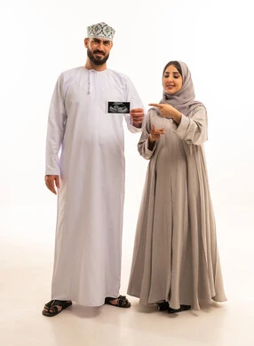 استخدام الأشعة فوق الصوتية لمتابعة الحمل، الاشارة باصبع السبابة بايماءات السعادة و السرور، بورترية لرجل عربي خليجي عماني يرتدي الدشداشة و الكمه يحمل اشعه السونار برفقه زوجته، الجسم بالطول الكامل، خلفية بيضاء
