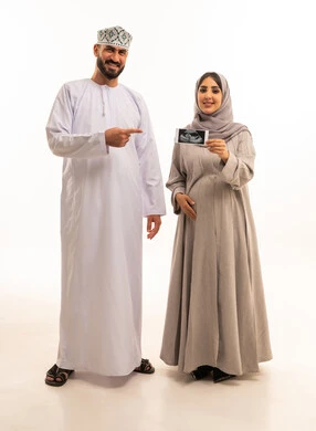 The use of ultrasound to monitor the fetus, a portrait of an Arab Gulf Omani pregnant woman wearing an abaya and hijab holding a sonogram in her hands accompanied by her husband, signaling with gestures of happiness and joy, full-body, white background.