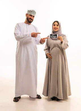 متابعة نمو الجنين من خلال الأشعة الصوتية، بورترية لامراه حامل عربيه خليجيه عمانية ترتدي العباءة و الحجاب تمسك بيديها اشعه السونار برفقه زوجها ، الاشارة بايماءات السعادة و السرور، الجسم بالطول الكامل، خلفية بيضاء