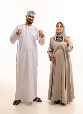 الاطمئنان على صحة الطفل، تعابير النجاح و تحقيق الاهداف، بورترية لامراه حامل عربيه خليجيه عمانية ترتدي العباءة و الحجاب تمسك بيديها اشعه السونار برفقه زوجها ، ايماءات السعادة و السرور، الجسم بالطول الكامل، خلفية بيضاء