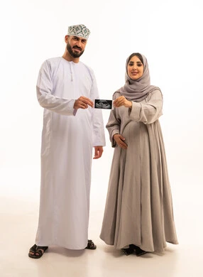 The concept of pregnancy and childbirth, the importance of fetal health, a portrait of an Arab Gulf Omani pregnant woman wearing a hijab and abaya standing with her husband holding an ultrasound image, reassurance about the child's health, full-body, white background.
