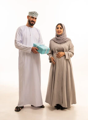 الألفة والمحبة بين الزوجين، مشاركة وتقديم الهدايا في الأعياد والمناسبات العائلية, بورتريه لرجل عربي خليجي عماني يرتدي الدشداشة و الكمة يقدم لزوجته صندوق الهديه، مفهوم الحمل و الانجاب, الجسم بالطول الكامل، خلفية بيضاء