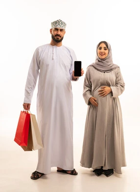 A blank black screen displayed on a mobile phone, a portrait of an Arab Gulf Omani man wearing a dishdasha and kumma carrying colorful paper bags accompanied by his wife, taking advantage of seasonal offers and discounts and Black Friday, the concept of pregnancy and childbirth, shopping from commercial malls, gestures of happiness and joy, full-body, white background.