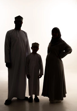 الترابط الأسري والحفاظ على الاستقرار العائلي، رعاية الآباء بأبنائهم والاهتمام بهم، مفهوم الحمل والانجاب، بورتريه لرجل عربي خليجي عماني يرتدي الدشداشة و الكمة يقف برفقة زوجته و ابنه ينظران  للكاميرا بإيماءات السعادة، صورة الجسم بالطول الكامل، خلفية بيضاء، سولوليت