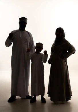 رعاية الآباء بأبنائهم والاهتمام بهم، تعابير الإعجاب والقبول، مفهوم الحمل والانجاب، بورتريه لرجل عربي خليجي عماني يرتدي الدشداشة و الكمة يقف برفقة زوجته و ابنه يشير باصبع الابهام للأعلى بهدف الرضا والموافقة، النظر للكاميرا بإيماءات السعادة، صورة الجسم بالطول الكامل، خلفية بيضاء، سولوليت