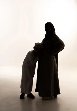 مفهوم الحمل والانجاب، النظر إلى الكاميرا بإيماءات الحماس، صورة ظلية لولد عربي خليجي عماني يرتدي الدشداشة و الكمة يضع اذنه على بطن والدته، مفهوم انتظار قدوم المولود، الجسم بالطول الكامل، خلفية بيضاء، سولوليت