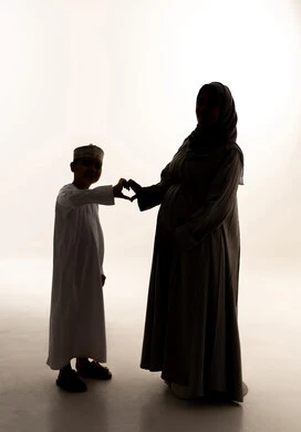 Love, affection, and connection, a silhouette of an Arab Gulf Omani mother wearing an abaya and hijab forming a heart shape with her hands with her son, the concept of motherhood and childhood, caring for and supporting children, full-body, white background, silhouette.