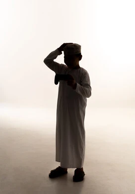 Gestures of loss and disappointment, a silhouette of an Arab Gulf Omani boy wearing a dishdasha and kumma holding a game controller with his hand on his head showing expressions of sadness and discontent, having a good time playing video games, enjoying modern technologies and gadgets, full-body, white background, silhouette.
