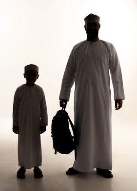 الشعور بالأمان والحب مع الآباء، موسم العودة للمدارس في السعودية، مفهوم الاعتناء بالأبناء والاهتمام بهم، صورة ظلية لرجل عربي خليجي عماني يرتدي الدشداشة و الكمة يمسك حقيبة الظهر برفقة ابنه، الاستعداد للعام الدراسي، الجسم بالطول الكامل، خلفية بيضاء ، سولوليت