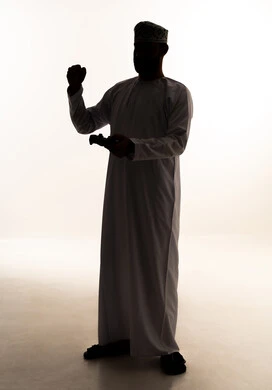 Raising a fist upwards with expressions of victory and winning, modern electronic entertainment devices and technologies, spending enjoyable and entertaining time, interacting and engaging with video games and PlayStation, a silhouette of an Arab Gulf Omani man wearing a dishdasha and kumma holding a game controller in his hands, full-body, white background, silhouette.