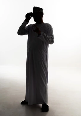 الاشارة الى شيء ما ، حب الاستكشاف و المغامرة، رؤية الاشياء البعيدة عبر التلسكوب, صورة ظلية لرجل عربي خليجي عماني يرتدي الدشداشة و الكمة يمسك بيدية منظار ثنائي العينين, صورة الجسم بالطول الكامل, خلفية بيضاء ، سولوليت