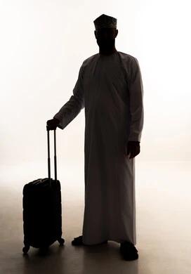 القيام بجولات ترفيهية في إجازة الصيف , مفهوم السياحة والسفر، صورة ظلية لرجل عربي خليجي عماني يرتدي الدشداشة و الكمة يحمل حقيبة السفر، الاستعداد لقضاء رحلة صيفية ممتعة, صورة الجسم بالطول الكامل، خلفية بيضاء ، سولوليت