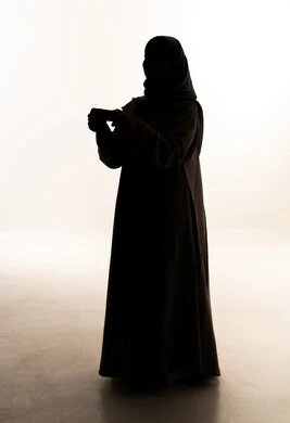 Interaction and immersion with video games and PlayStation, modern electronic entertainment devices and technologies, spending enjoyable and entertaining time, a silhouette of an Arab Gulf Saudi woman wearing an abaya and hijab holding a game controller in her hands, full-body, white background, silhouette.