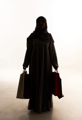 Gestures of joy after shopping and purchasing and their positive impact on women, seasonal offers and discounts in Saudi markets, a silhouette of an Arab Gulf Saudi woman wearing an abaya and hijab holding colorful shopping bags in her hand, full-body image, white background, silhouette.