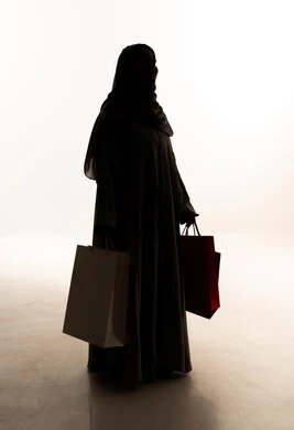 Seasonal offers and discounts in Saudi markets, looking at something, gestures of joy after shopping and buying and its positive impact on women, a silhouette of an Arab Gulf Saudi woman wearing an abaya and hijab holding colorful shopping bags in her hand, full-body image, white background, silhouette. Seasonal offers and discounts in Saudi markets, looking at something, gestures of joy after shopping and buying and its positive impact on women, a silhouette of an Arab Gulf Saudi woman wearing an abaya and hijab holding colorful shopping bags in her hand, full-body image, white background, silhouette.