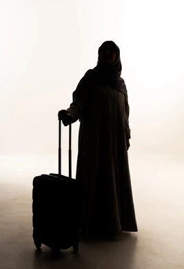 Enjoying tourist trips during the holiday, looking at something, preparing for enjoyable travels, a silhouette of an Arab Gulf Saudi woman wearing an abaya and hijab holding a travel bag in her hand, full-body, white background, silhouette.
