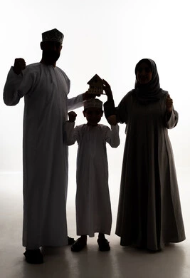 Success and achieving goals, strong family ties, the pursuit of owning a new home, buying and selling real estate, a silhouette of an Arab Gulf couple from Oman wearing traditional attire holding a small wooden model of a house with their son, gestures of joy and happiness, full-body, white background, silhouette.