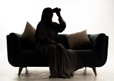 Seeing distant things through a telescope, a love for exploration and adventure, a silhouette of an Arab Gulf Saudi woman wearing an abaya and hijab sitting on a sofa holding binoculars in her hands, white background, silhouette.