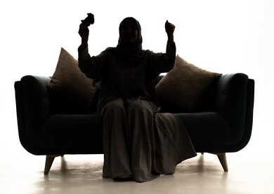 رفع قبضة اليد للاعلى بتعابير الفوز و الربح, اجهزة وتقنيات الكترونية حديثة ترفيهيه, قضاء وقت ممتع ومسلي، التفاعل والاندماج مع ألعاب الفيديو والبلايستيشن،,  صورة ظلية لامراة عربيه خليجيه سعودية تجلس على الاريكة تمسك بيديها عصا التحكم ، خلفية بيضاء، سولوليت