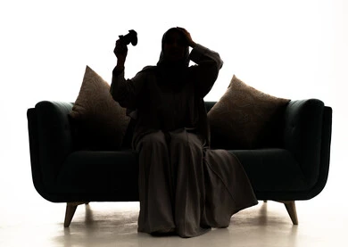 Gestures of loss and disappointment, a silhouette of a Saudi Arabian Gulf woman sitting on the couch holding a game controller with her hands on her head showing expressions of sadness and discontent, having a good time playing video games, enjoying modern technologies and gadgets, white background, silhouette.
