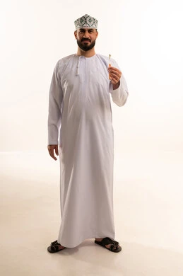 The concept of healthy habits, maintaining and continuously cleaning teeth, a bright white smile, daily oral hygiene routine, avoiding cavities and gum diseases, a portrait of an Arab Omani Gulf man wearing a dishdasha and kumma holding a toothbrush in his hands, full body, white background.