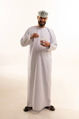 Daily ear cleaning routine, care and attention to ear health, use of cotton swabs and sticks, portrait of an Arab Omani Gulf man wearing a dishdasha and kumma holding a cotton swab in his hands, attention to external appearance, full-body, white background.