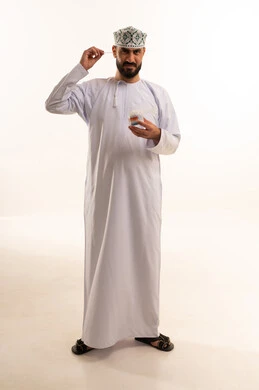 استخدام أعواد ونكاشات القطن، العناية والاهتمام بصحة الأذن، روتين نظافة الأذنين اليومية، بورتريه لرجل عربي عماني خليجي يرتدي الدشداشة و الكمة يمسك بيدية نكاشة قطنية, الاهتمام بالمظهر الخارجي, الجسم بالطول الكامل، خلفية بيضاء