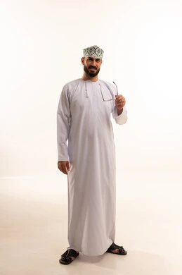 الرؤية من خلال النظارة الطبية ، بورتريه لرجل عربي عماني خليجي يرتدي  الدشداشة و الكمة يمسك بيده نظاره طبيه, النظارة الطبية الخاصة بضعف النظر، مفهوم طول النظر، الجسم بالطول الكامل، خلفية بيضاء