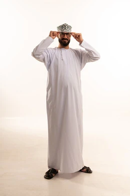 مفهوم تحسين الرؤية ومحاولة تعديل البصر، الاهتمام بالمظهر الخارجي، ارتداء النظارات الخاصة بضعف النظر،بورتريه لرجل عربي خليجي عماني يرتدي الدشداشة والكمة يضع على وجهه نظارة طبية, الجسم بالطول الكامل، خلفية بيضاء