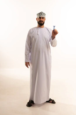 لمسة نظافة تمنح انتعاشًا وثقة, الحفاظ على الأناقة، العناية بالبشرة والاهتمام بالمظهر الخارجي، بورتريه لرجل عربي خليجي عماني يرتدي  الدشداشة و الكمة يمسك شفرة حلاقة، الجسم بالطول الكامل، خلفية بيضاء