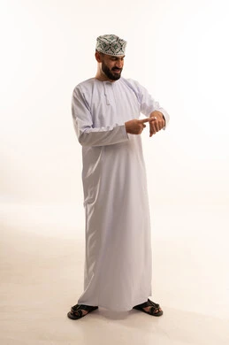 ترطيب وتنظيف وتفتيح الجلد، روتين العناية بالبشرة ، مفهوم الإهتمام بنضارة وتحسين البشرة، استخدام مكونات تجميلية شبابية، بورتريه لرجل عربي خليجي عماني يرتدي الدشداشة والكمة يضع كريم المرطب على يديه ، الجسم بالطول الكامل، خلفية بيضاء