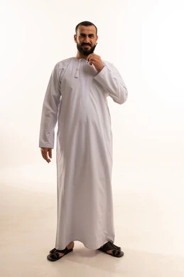 مفهوم العناية والاهتمام بالجمال والأناقة والمظهر الخارجي، بورتريه دلرجل عربي خليجي سعودي  يرتدي الثوب الابيض يقوم بتمشيط ذقنه باستخدام ( المشط )، تعابير وإيماءات تدل على السعادة والسرور، الجسم بالطول الكامل، خلفية بيضاء